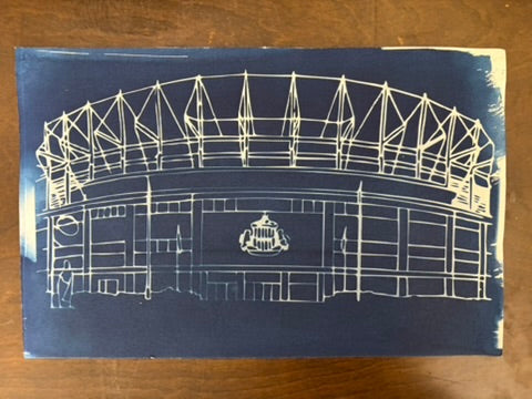 A vintage blue ink cyanotype print of th the stadium of light,  placed on a wooden surface.